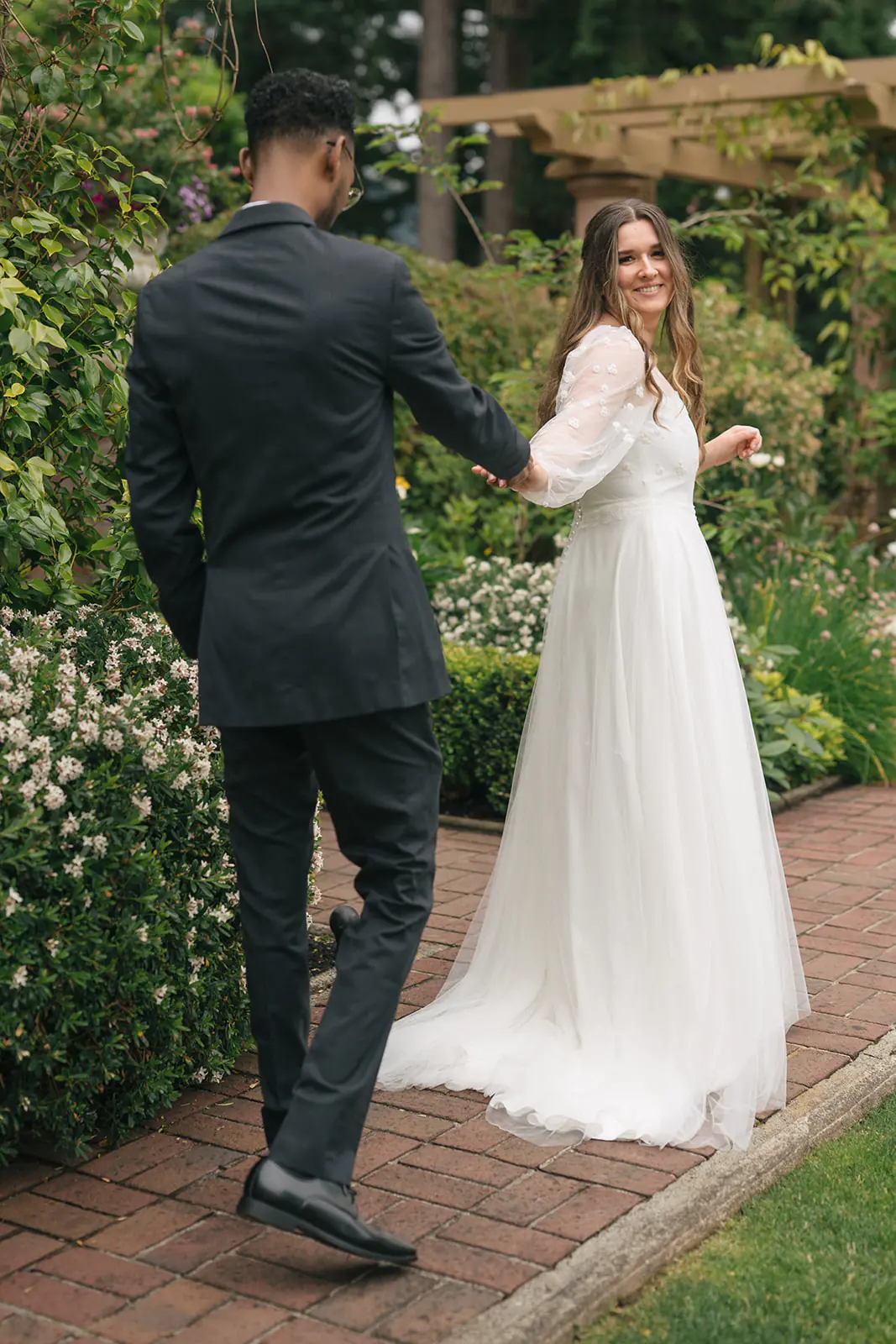 Bride leading groom by the hand along a brick garden path at Lairmont Manor.