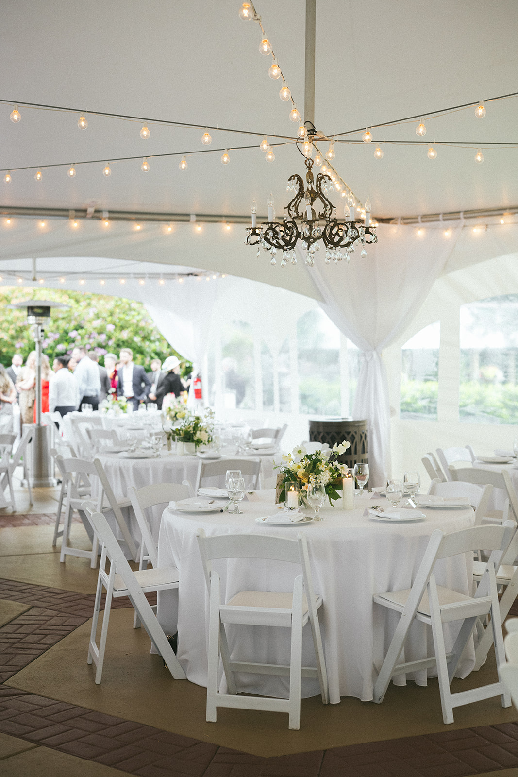 Elegant reception tables with white linens and floral centerpieces inside a wedding tent