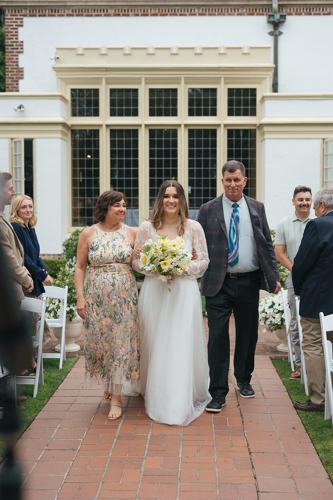 Bride smiling while being escorted down the aisle by her parents at Lairmont Manor wedding
