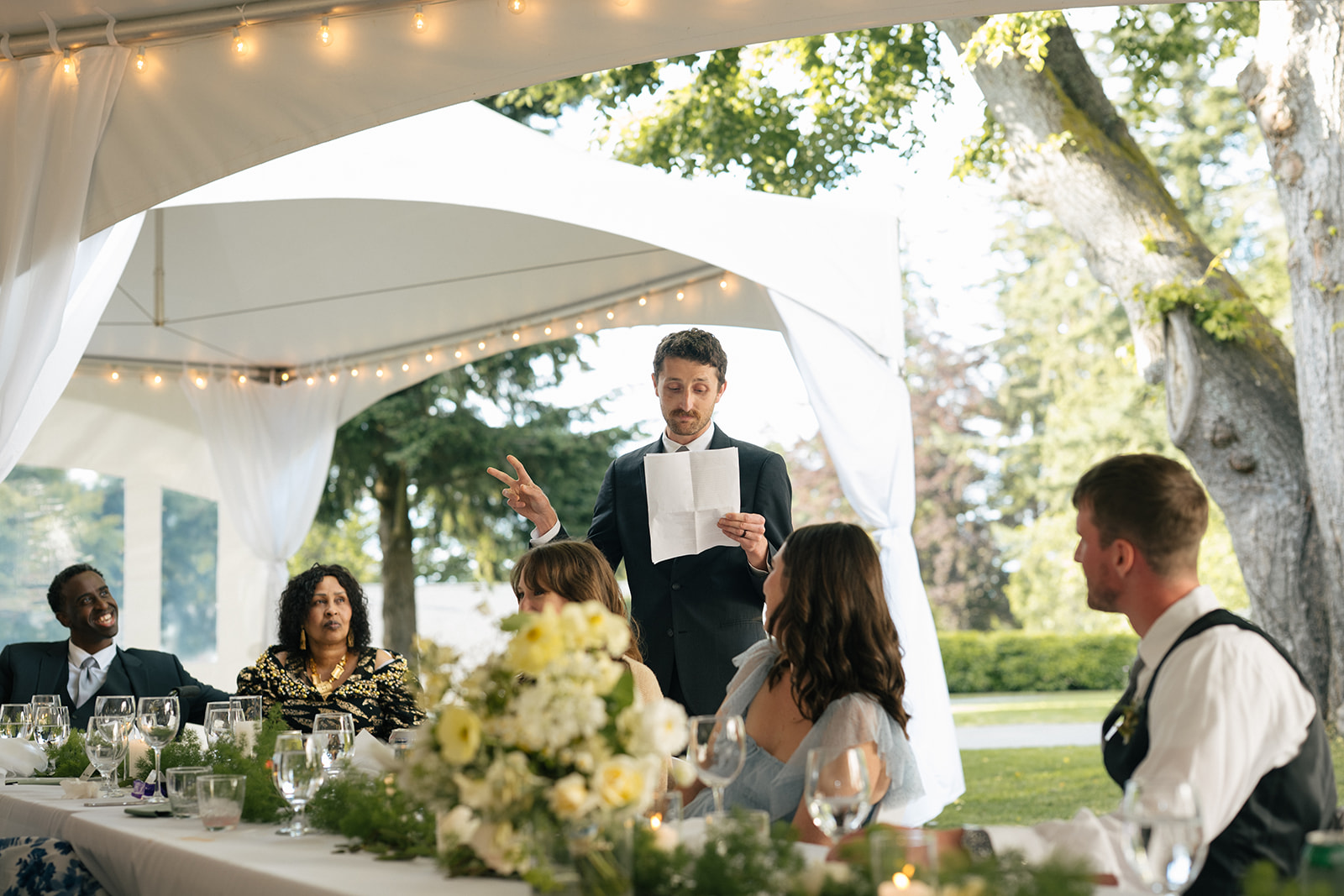 Wedding guest giving a speech at the head table inside a white reception tent at Lairmont Manor