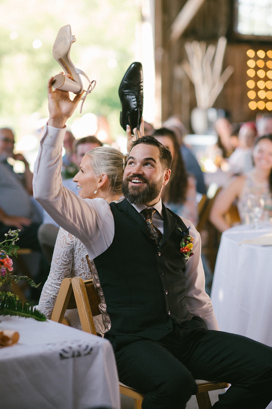 Groom laughs while holding up his own shoe and the bride's during the shoe game