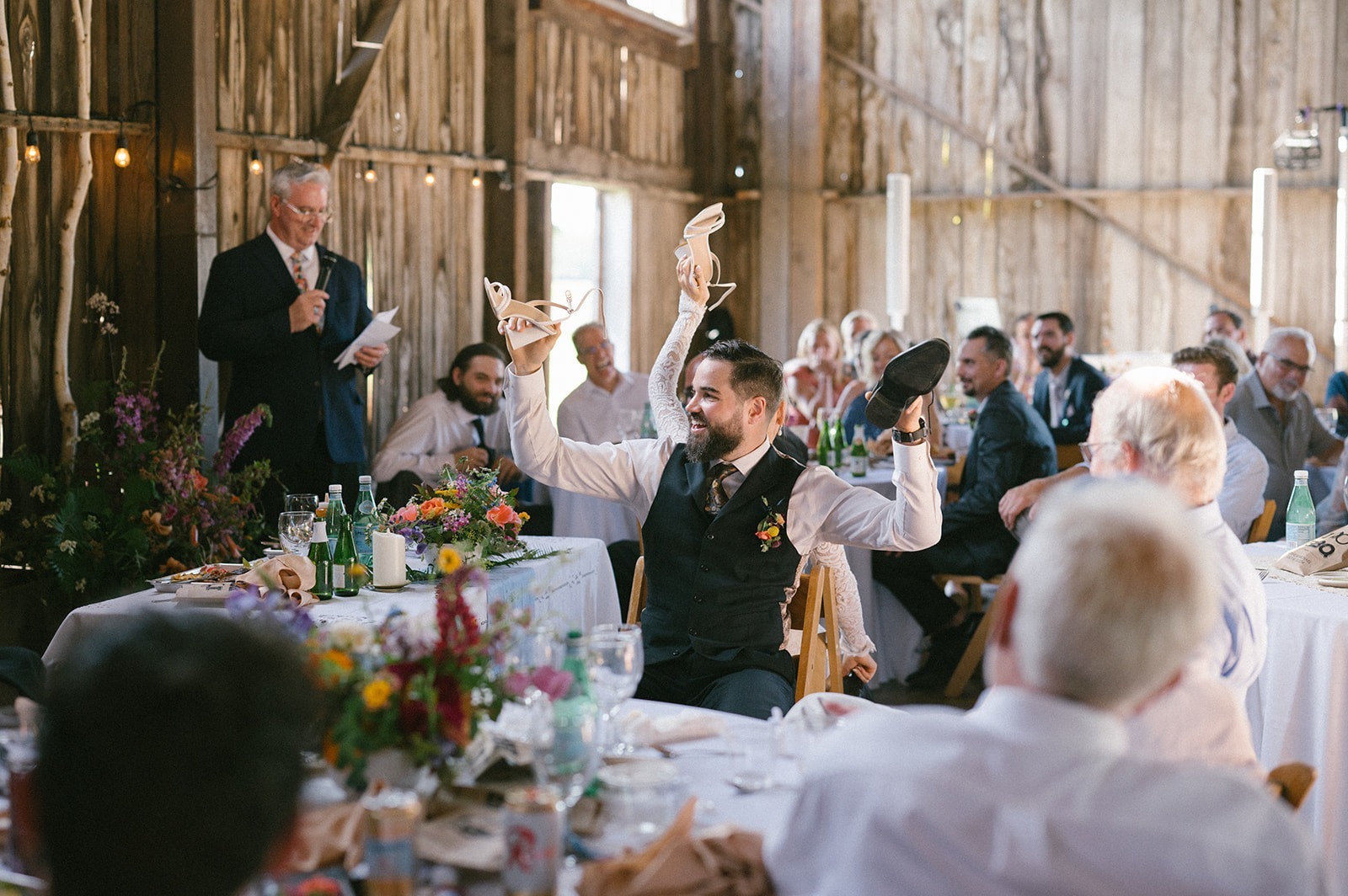 Guests watch from round dinner tables as the groom raises a shoe overhead