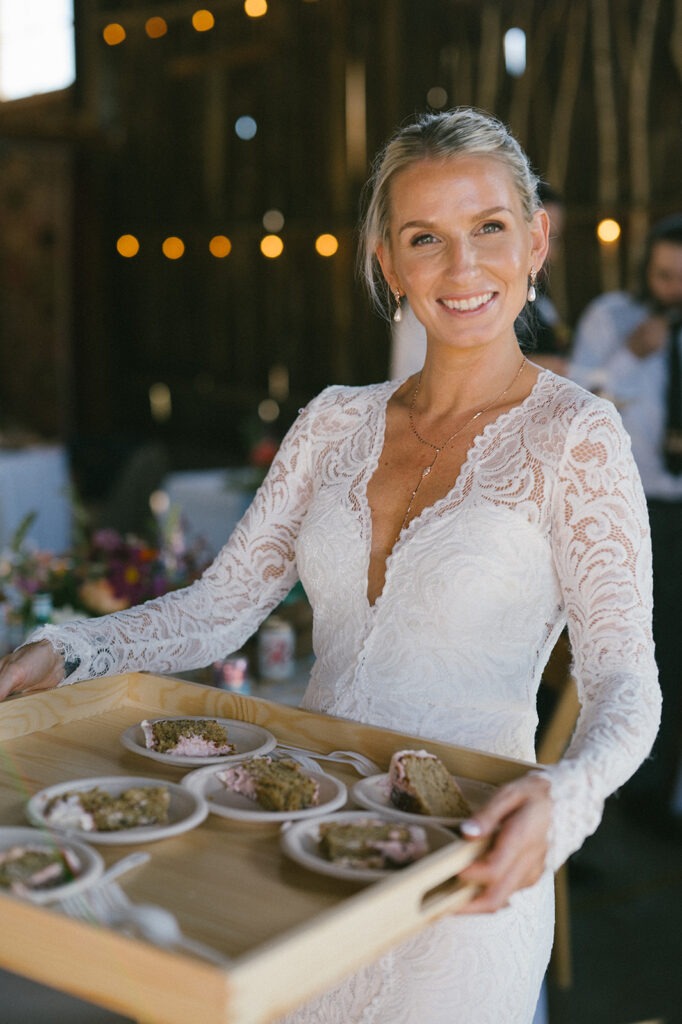 Bride smiles while carrying a wooden tray of dessert plates to guests