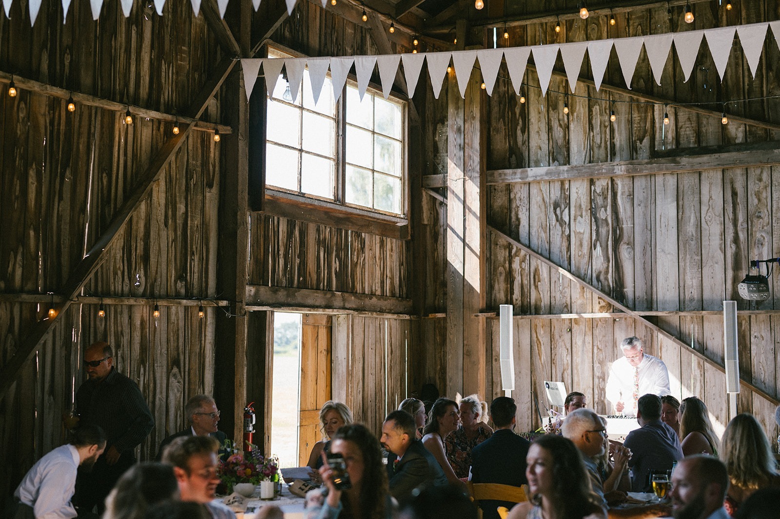 Guests fill round tables inside the barn as a DJ sets up in the background