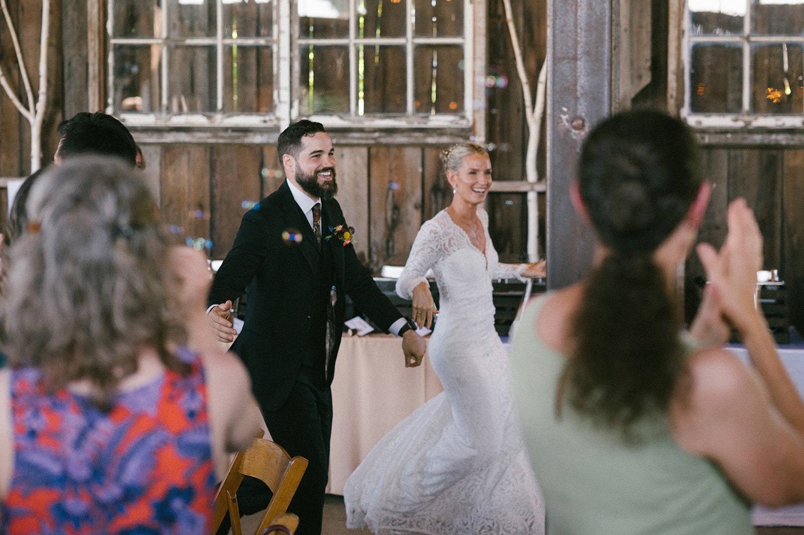 Newlyweds walk hand in hand into the reception as guests clap on both sides