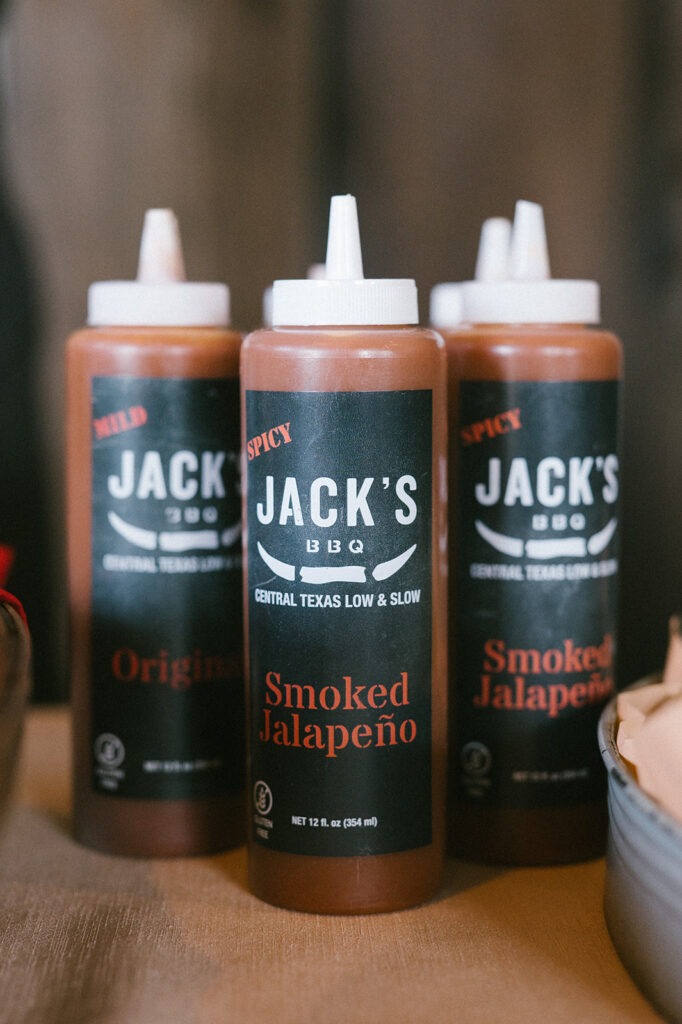 Bottles of Jack's BBQ sauce, mild and smoked jalapeño, sit ready for this Saltbox Barn wedding reception