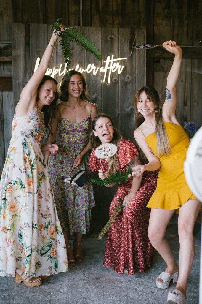 Four friends pose playfully with photo booth props under a neon sign