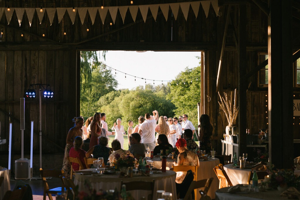 Guests dance together just inside the barn's open doors at sunset