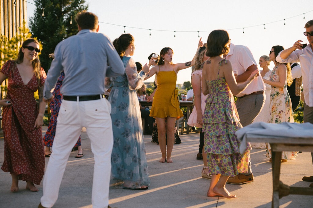 Guests dance outdoors under string lights at this Saltbox Barn wedding reception