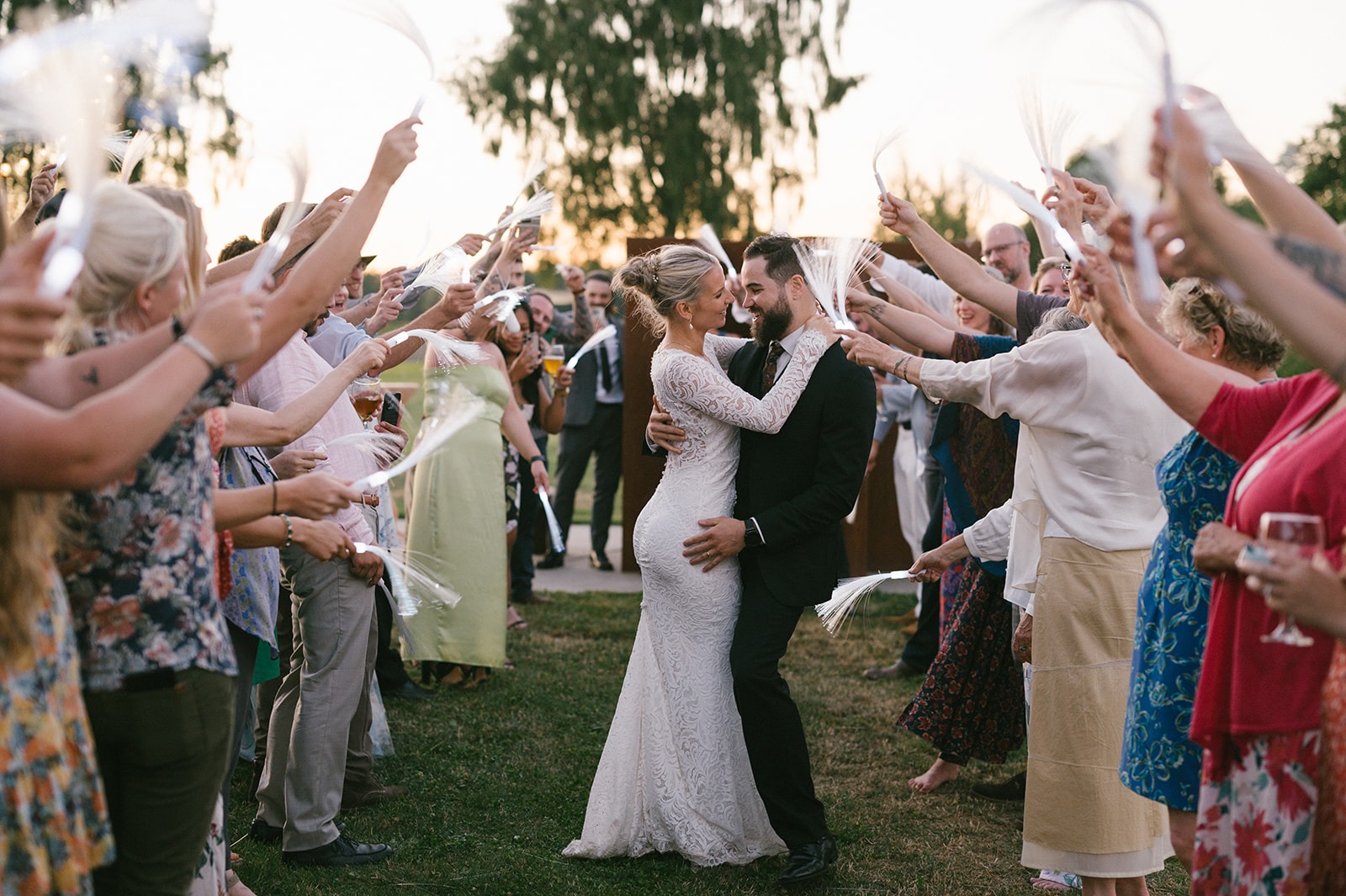 Guests surround the newlyweds, raising ribbon wands overhead in celebration