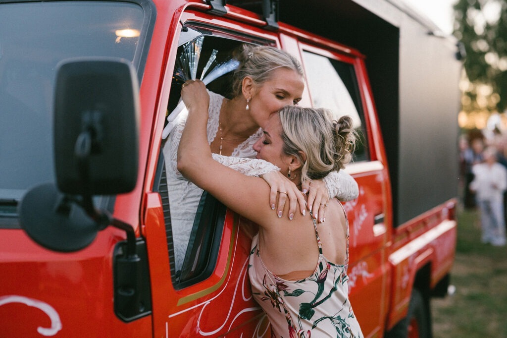 Bride leans out of the getaway truck to share a kiss with her sister before driving off