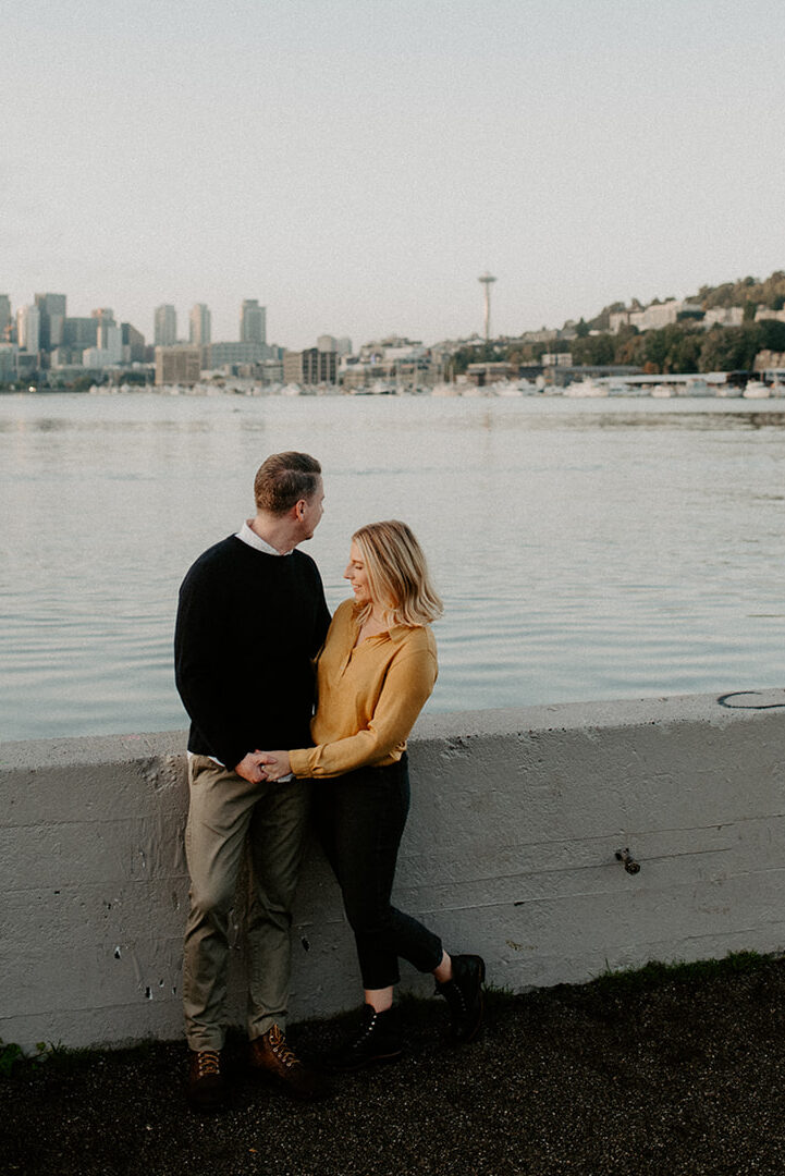 Couple leaning against a waterfront wall with Seattle skyline views