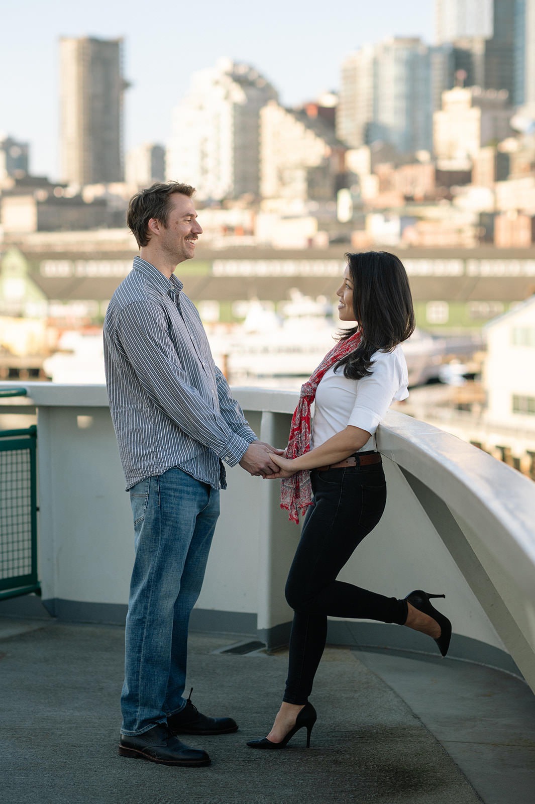 Couple holding hands on the Washington State Ferry with Seattle waterfront buildings blurred in the background