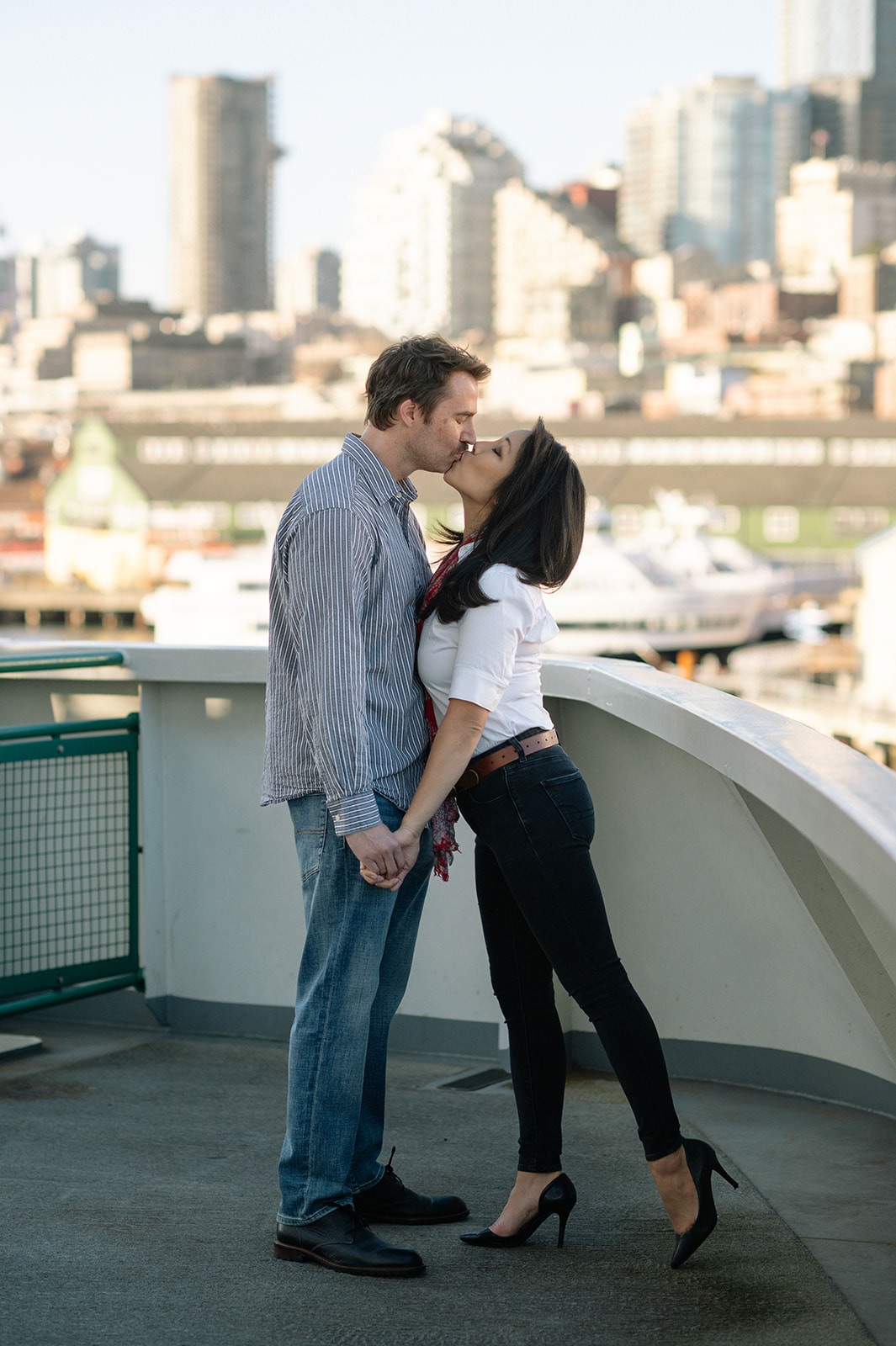 Couple sharing a kiss on the Washington State Ferry with Seattle skyline softly blurred behind them