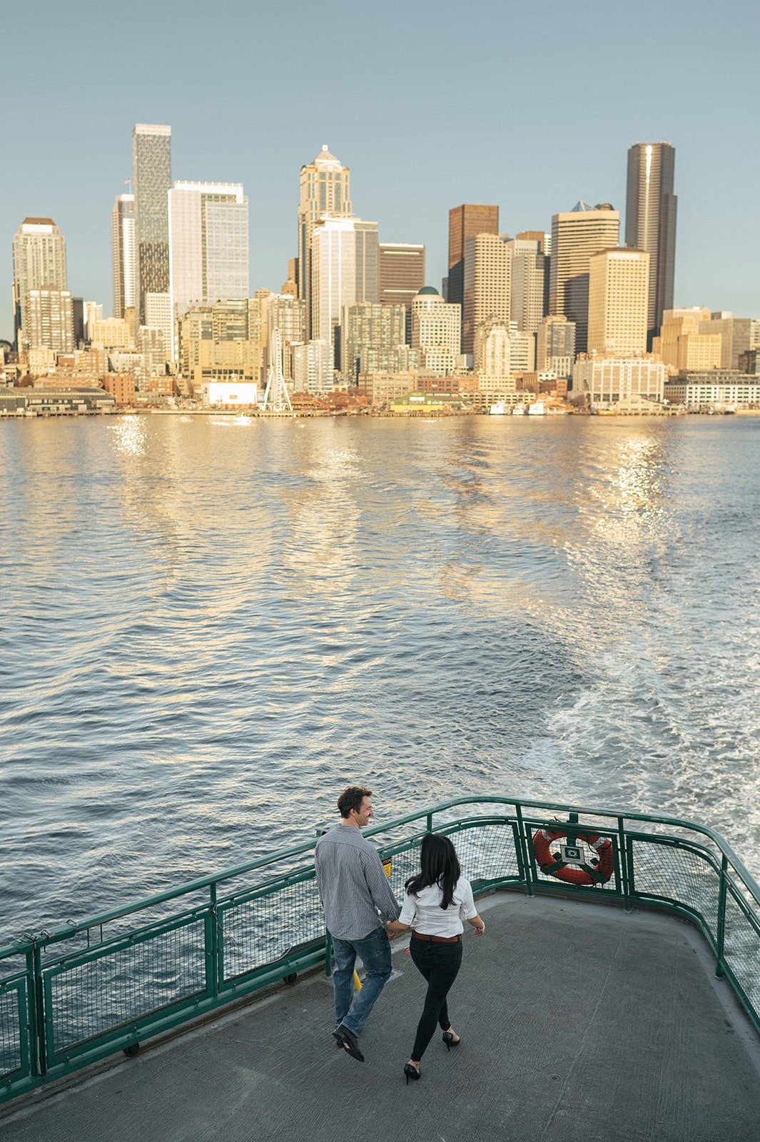 Couple walking together on the back of a Washington State Ferry with the Seattle skyline and water behind them