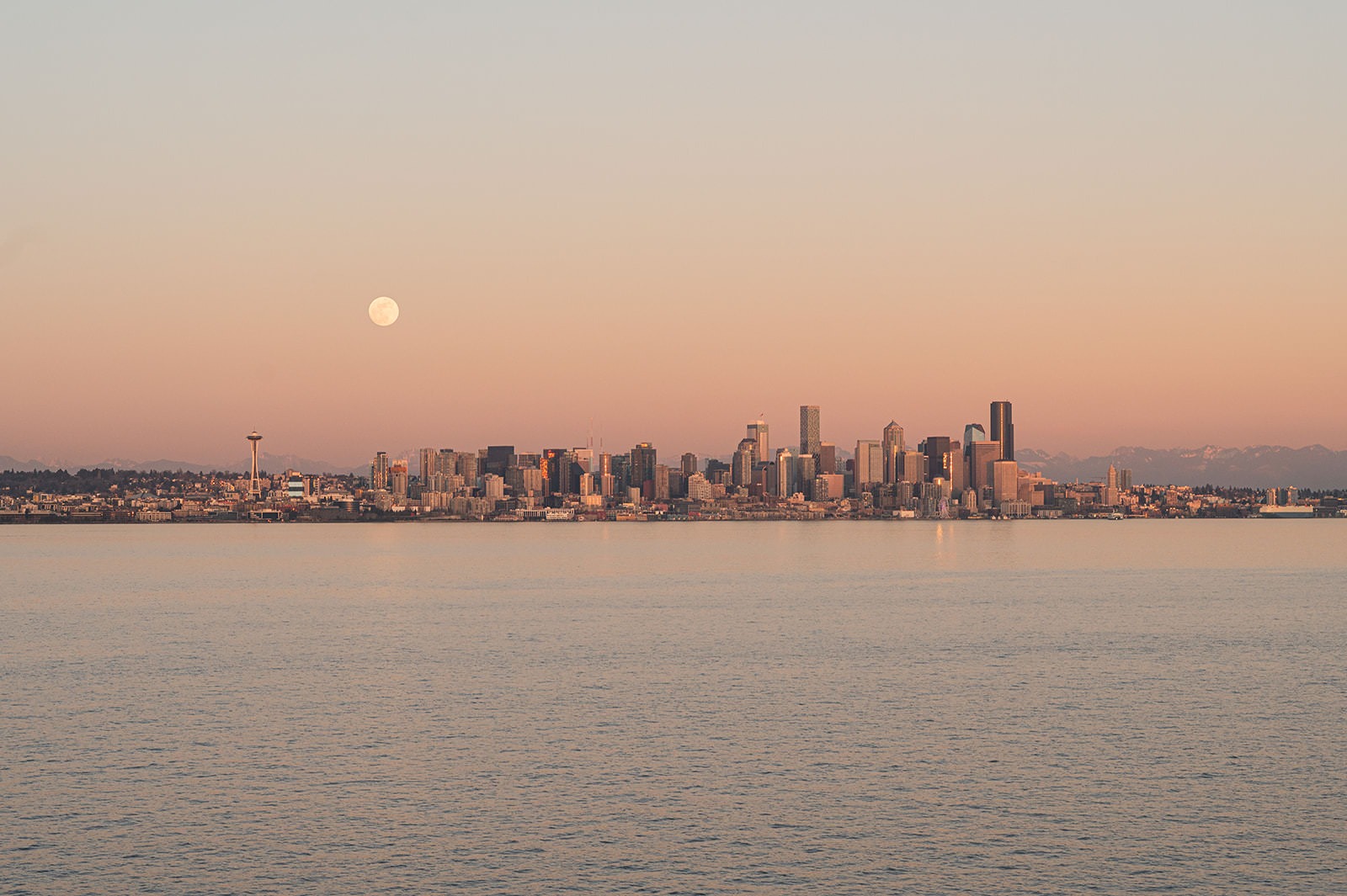 Seattle skyline across the water at sunset with a pale moon above the city
