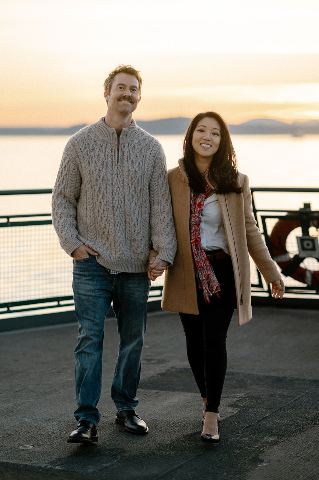 Couple walking hand in hand on the ferry deck at sunset during an engagement session