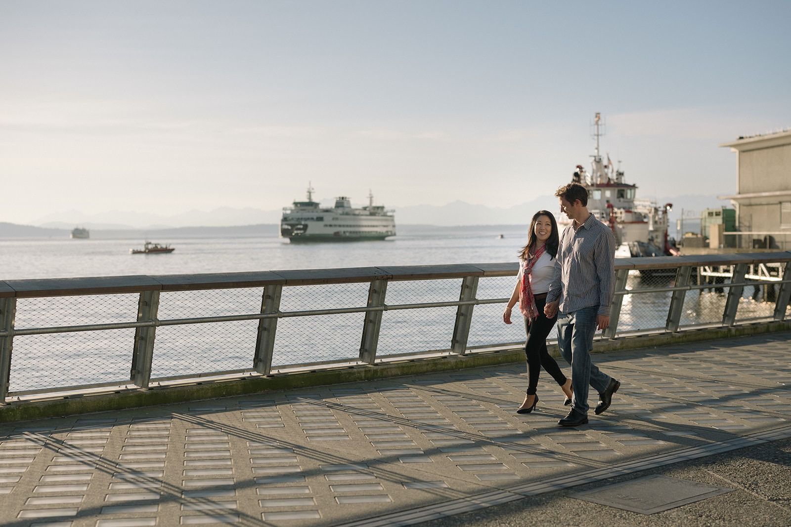 Couple walking along the Seattle waterfront with a Washington State Ferry in the background during an engagement session