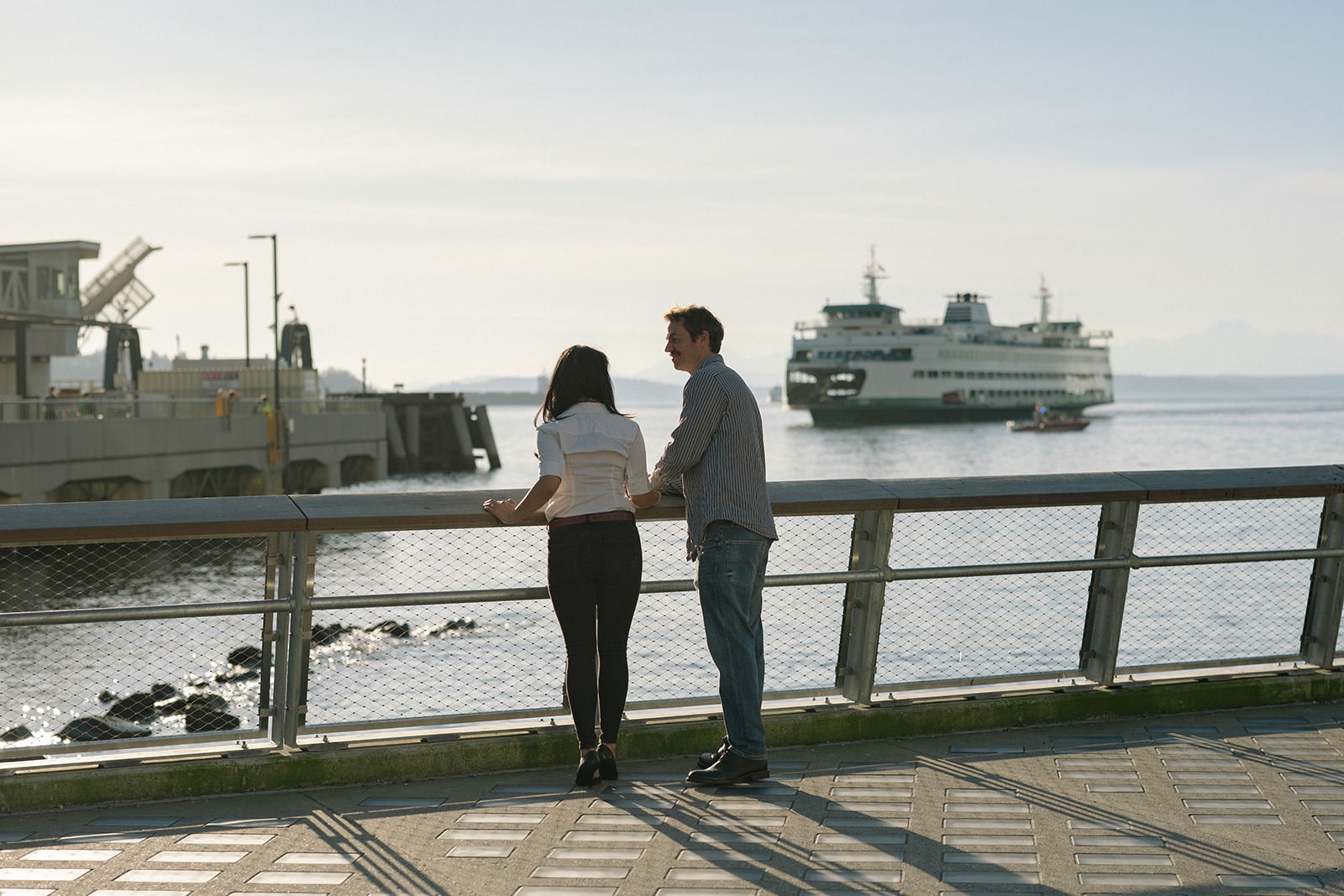 Couple standing by the Seattle waterfront railing with a Washington State Ferry in the background
