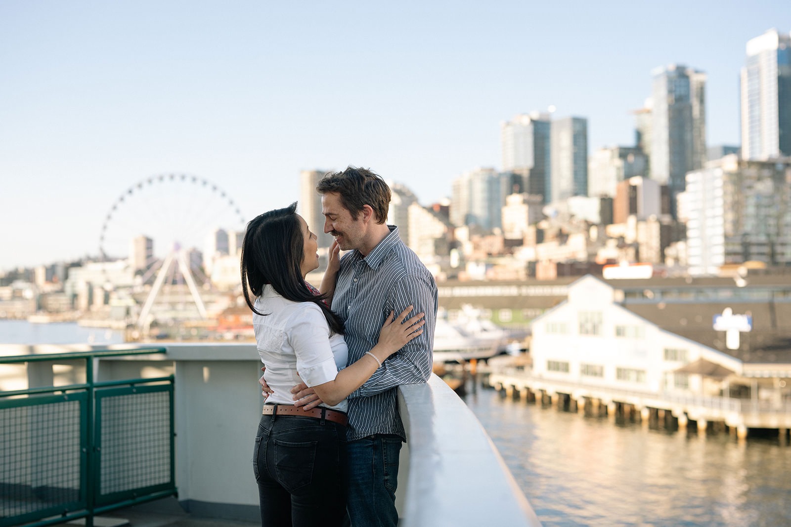 Couple embracing on the Washington State Ferry with the Seattle skyline in the background during an engagement session