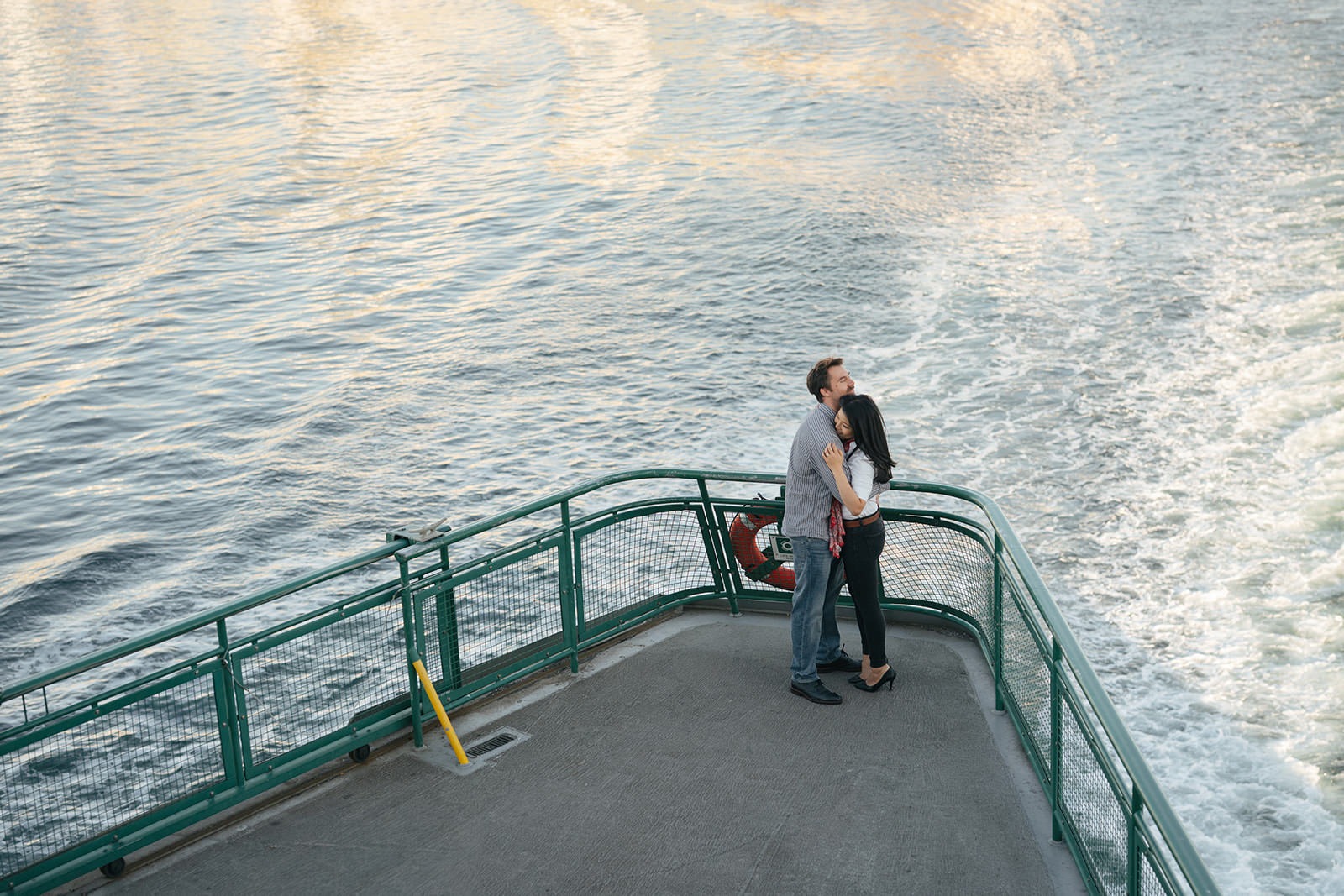 Overhead photo of a couple embracing on the back deck of a Washington State Ferry surrounded by water