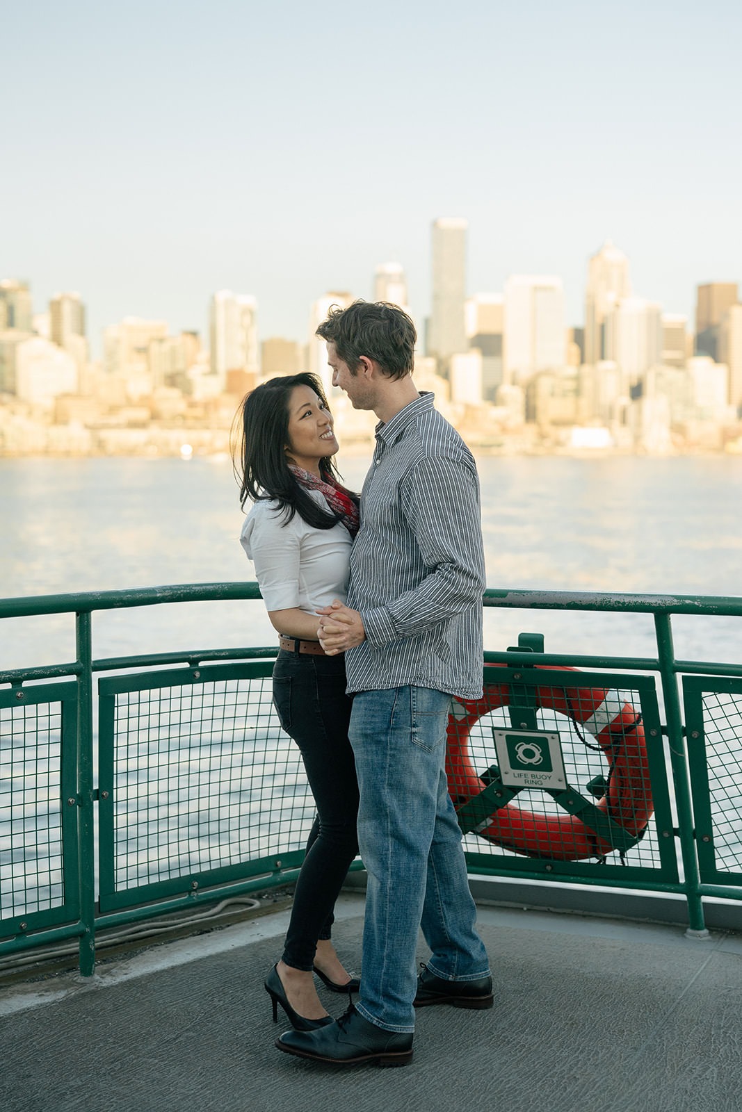 Couple standing together on the ferry deck with Seattle skyline views during a sunset engagement session