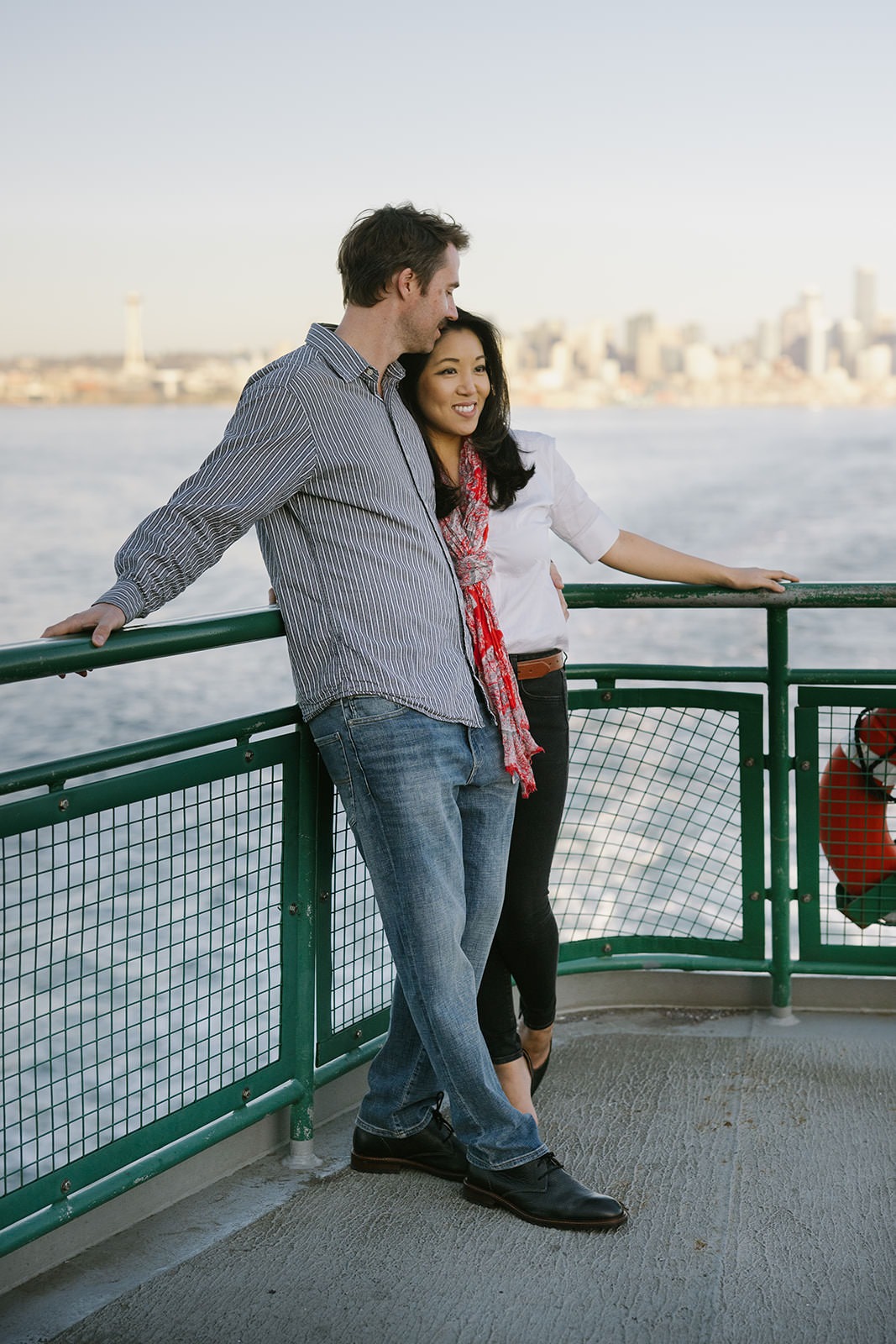 Couple leaning against the ferry railing with water and the Seattle skyline in the background