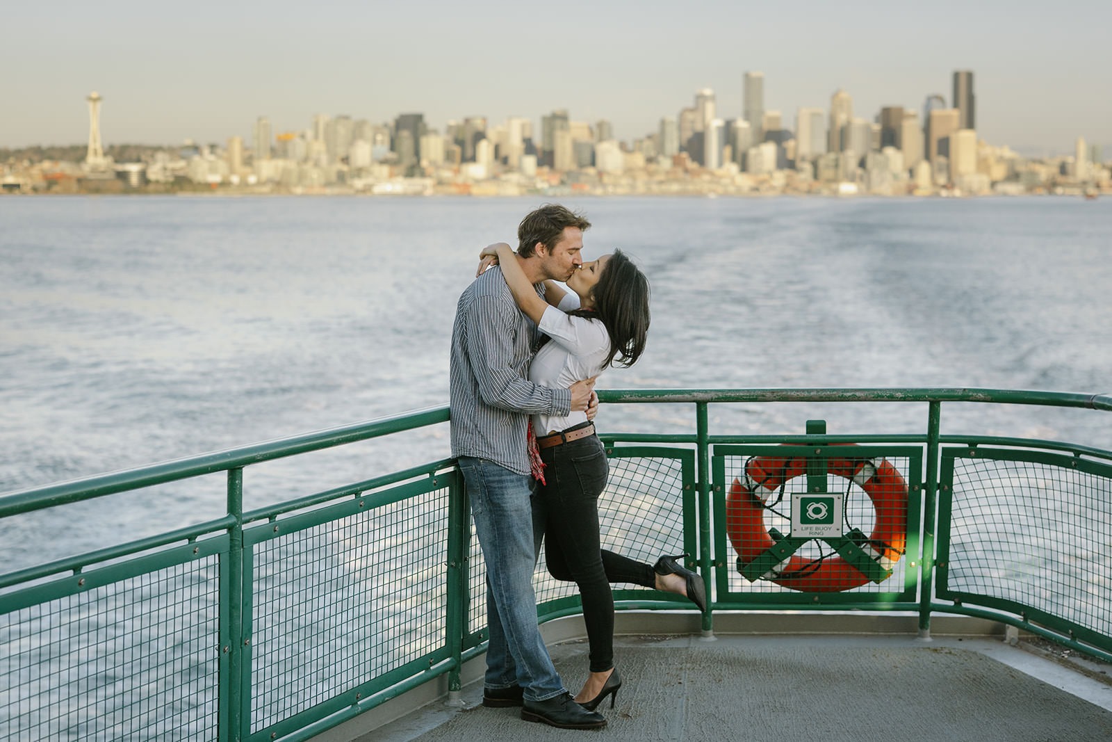 Couple kissing on the back of a Washington State Ferry with the Seattle skyline across the water