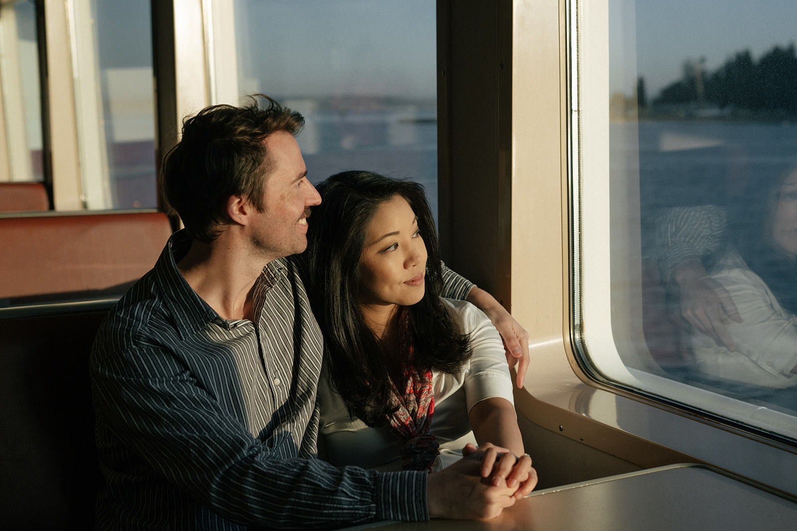 Couple sitting by the ferry window and looking out at the water during an engagement session