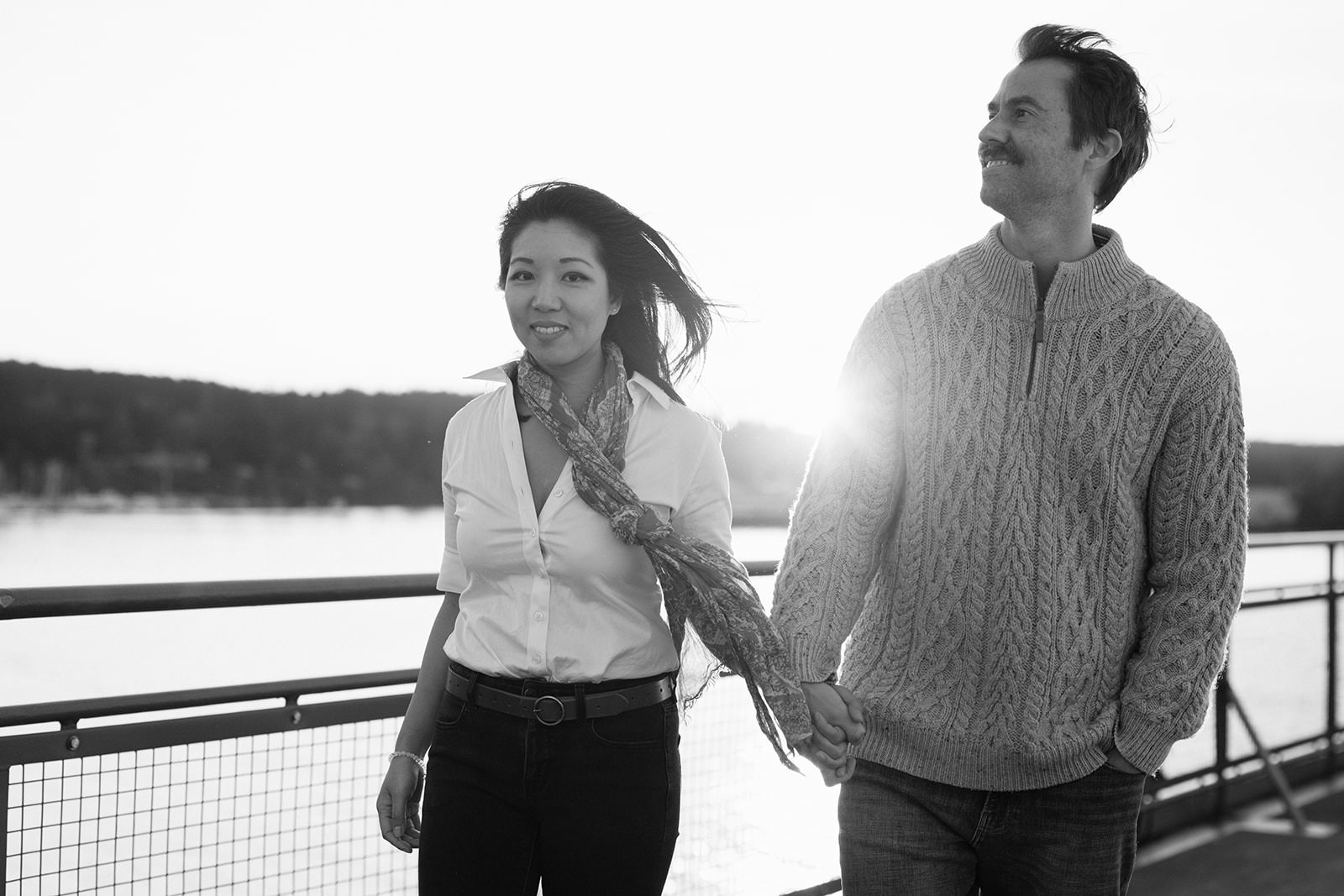 Black and white photo of a couple walking hand in hand on the ferry deck at sunset