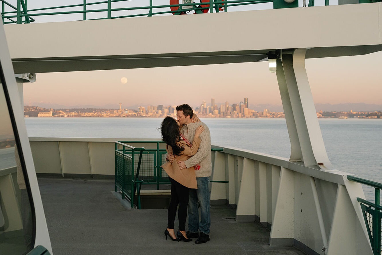 Couple kissing on the upper deck of a Washington State Ferry with the Seattle skyline in the distance