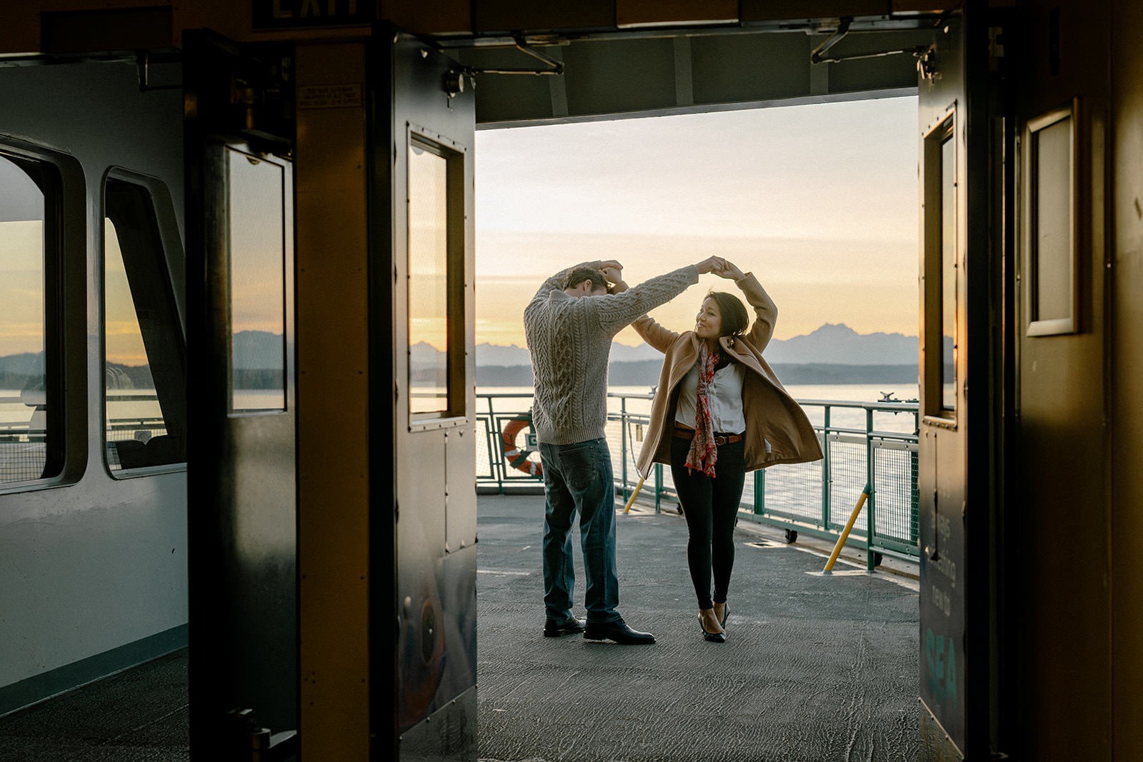 Couple twirling together in the ferry doorway at sunset during an engagement session