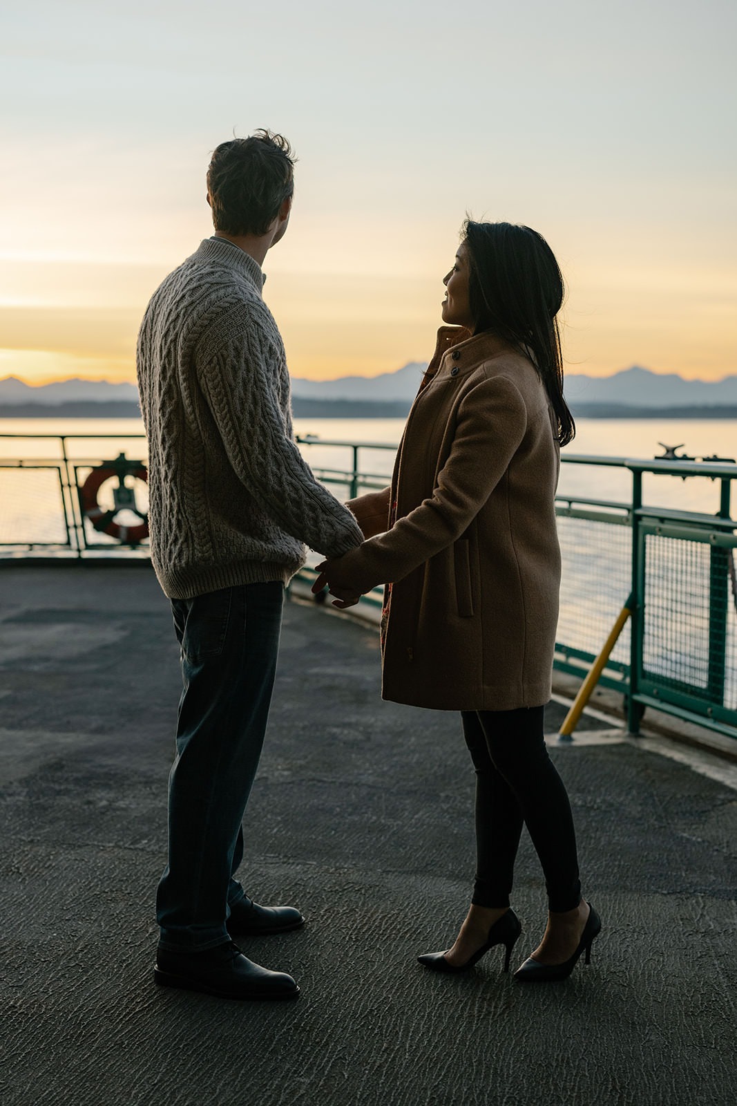 Couple holding hands on the ferry deck while looking toward the sunset and distant mountains