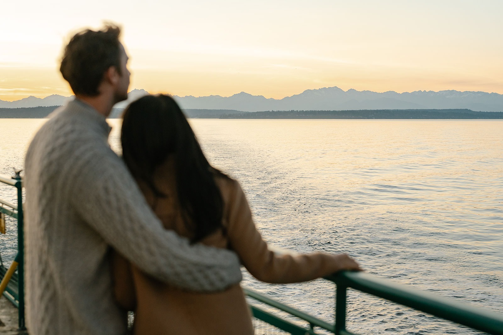 Couple embracing by the ferry railing while looking out across the water at sunset