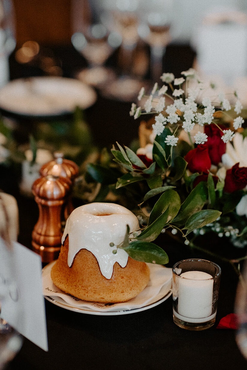 A bundt-style wedding cake with white icing drip surrounded by candles on the reception dessert table