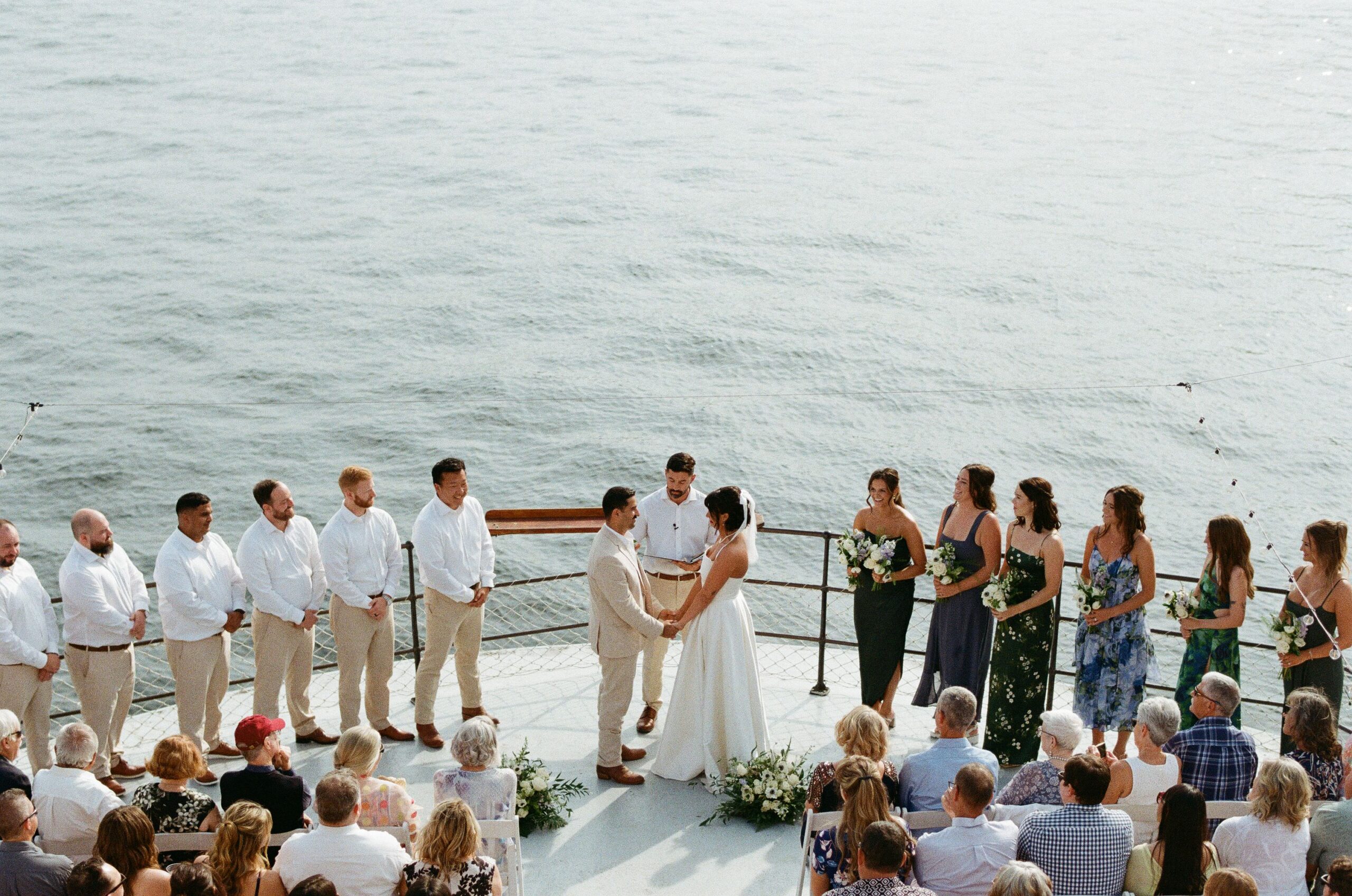 Aerial view of a wedding ceremony on the bow of MV Skansonia with guests seated and the lake behind the couple