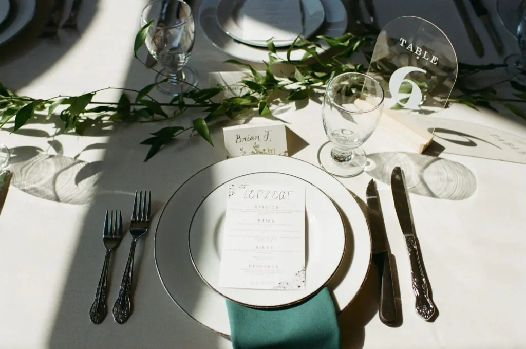 Wedding reception place setting detail on MV Skansonia with a menu card, greenery runner, acrylic table number, and teal napkin