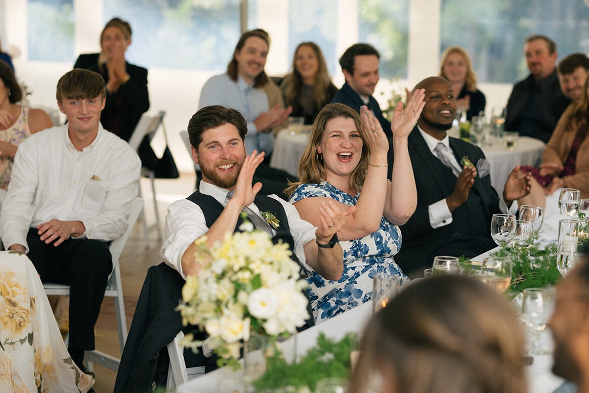 Wedding guests applauding during reception speeches inside a tent at Lairmont Manor