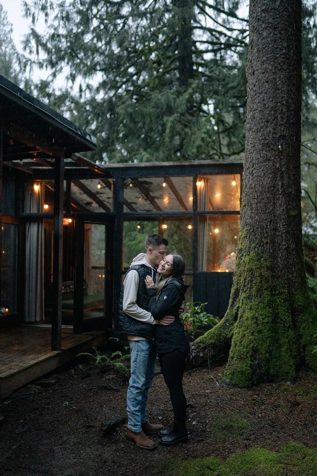 Groom-to-be kisses his fiancée on the temple outside their glowing cabin at Canyon Creek Cabins in Granite Falls, WA

