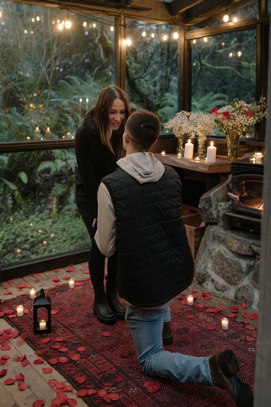 Groom-to-be kneels inside the candlelit glass sunroom for a Granite Falls cabin proposal