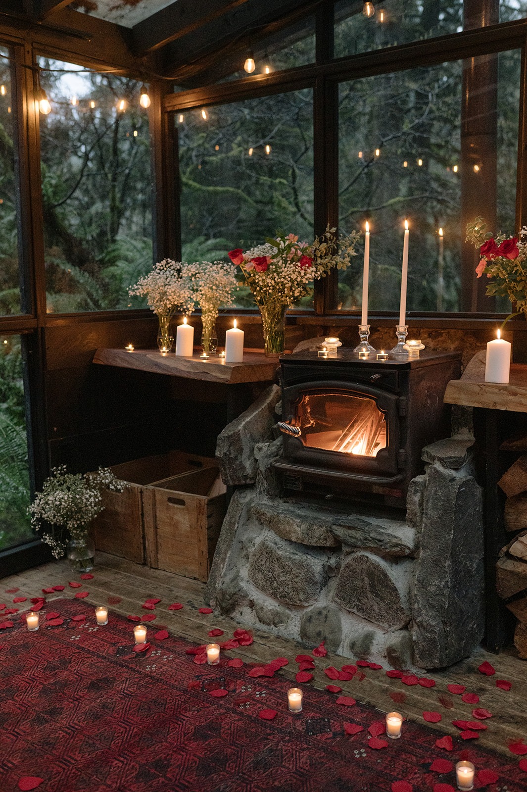 Wood stove surrounded by candles, red rose petals, and string lights inside the glass sunroom at Canyon Creek Cabins

