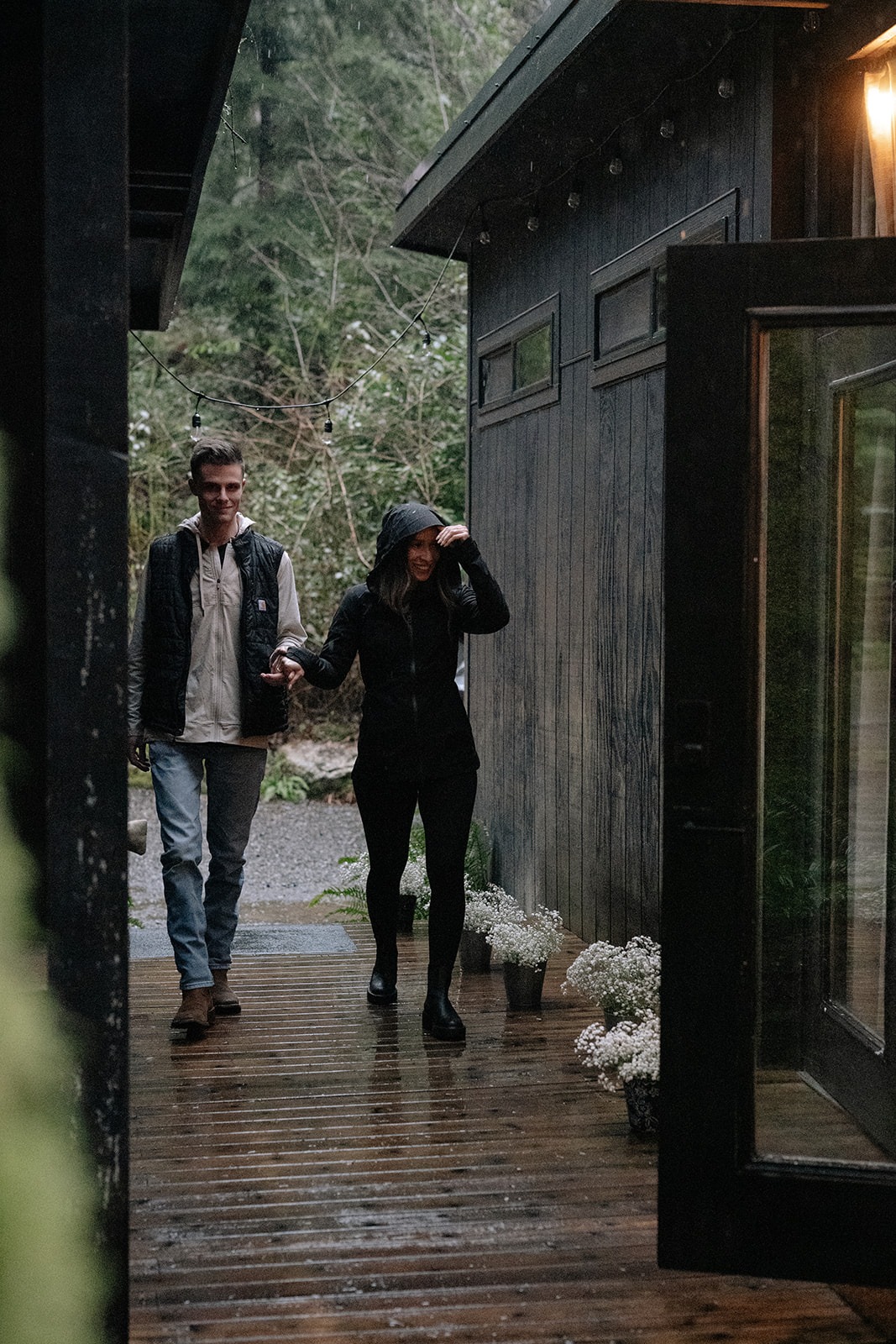 Couple walks hand in hand up the wet deck toward their rainy Canyon Creek Cabins proposal in Granite Falls