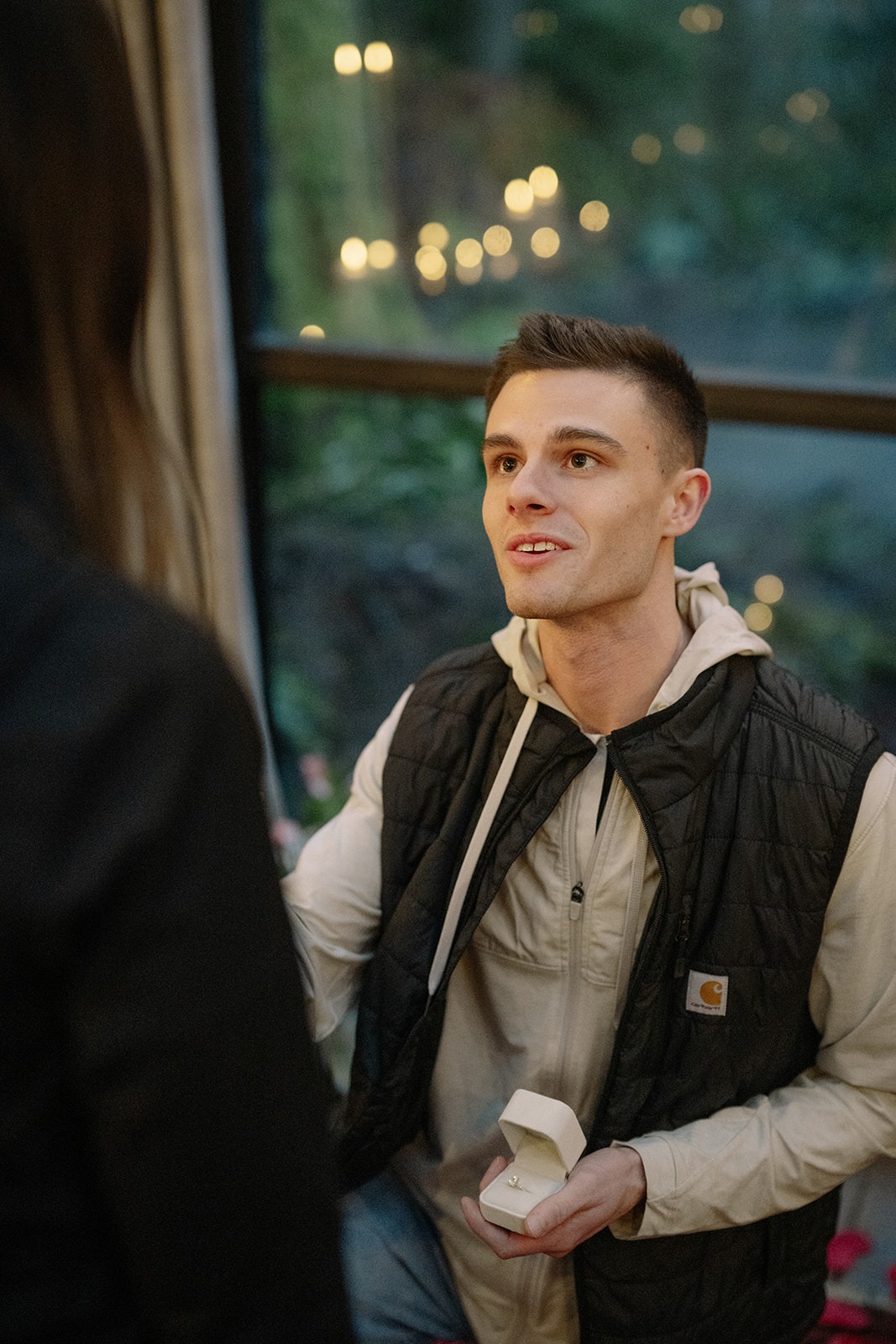 The moment of the proposal — he holds the open ring box inside the candlelit sunroom at Canyon Creek Cabins