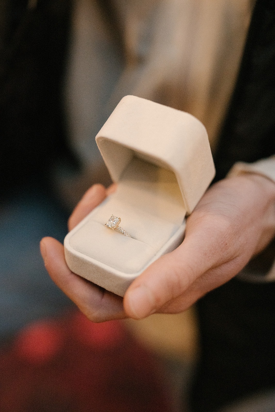 Emerald-cut diamond engagement ring in a cream velvet ring box during a rainy cabin proposal at Canyon Creek Cabins