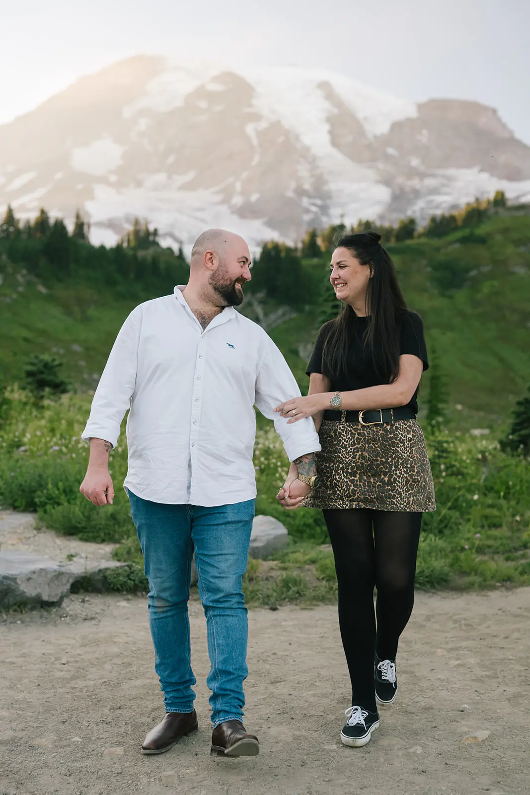 Newly engaged couple walks hand in hand down the Paradise trail with Mount Rainier behind them