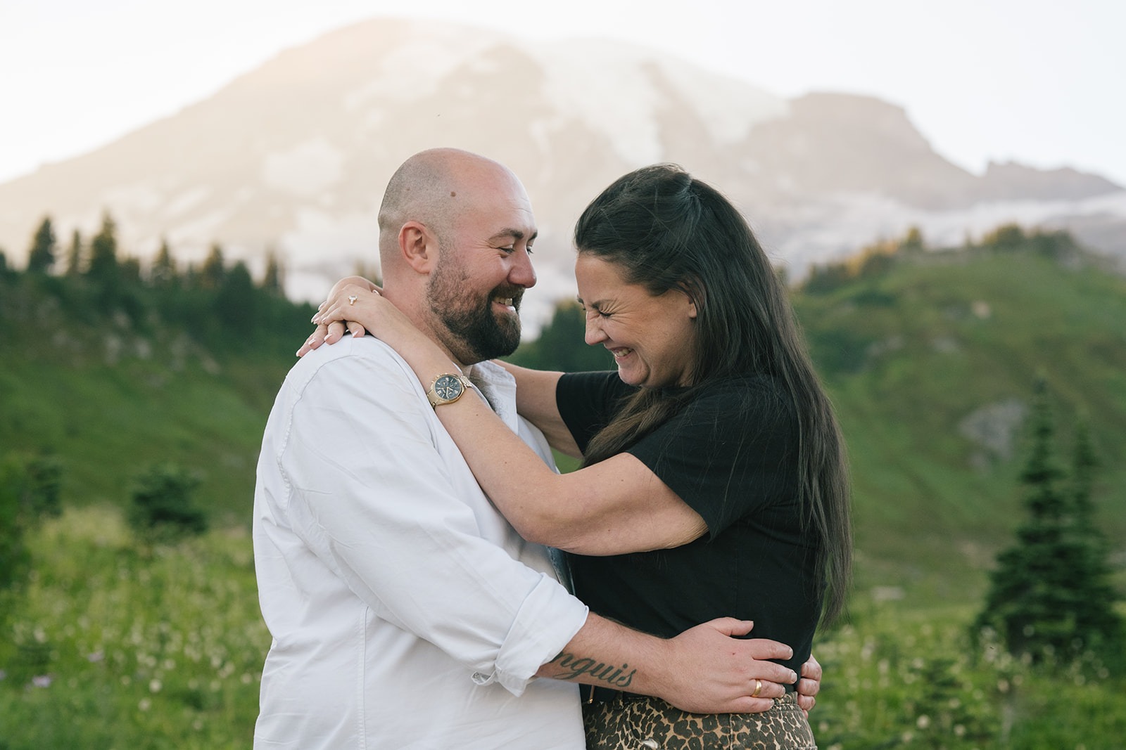 Newly engaged couple laughs together with Mount Rainier behind them after a surprise Mount Rainier proposal