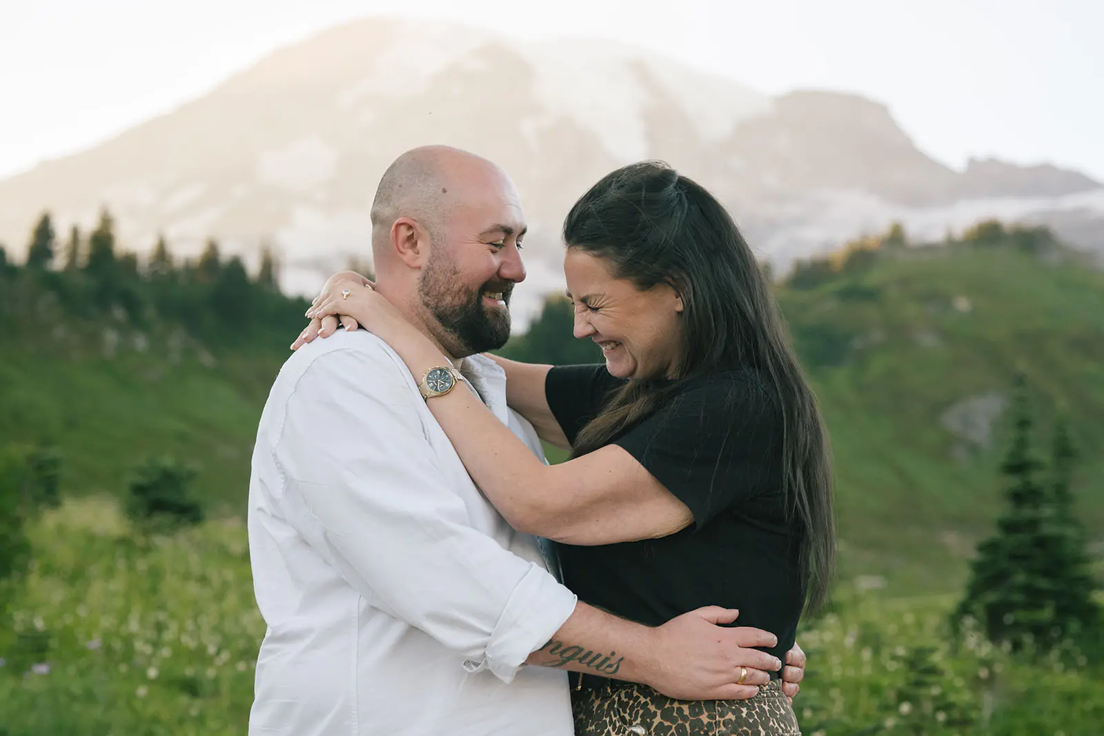 Newly engaged couple laughs together with Mount Rainier behind them after a surprise Mount Rainier proposal
