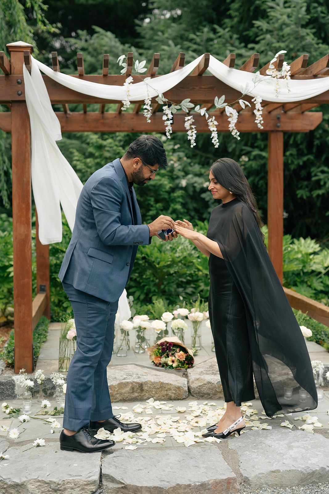 Piyush slides the engagement ring onto Priyanka's finger under the wisteria arch at Willows Lodge in Woodinville