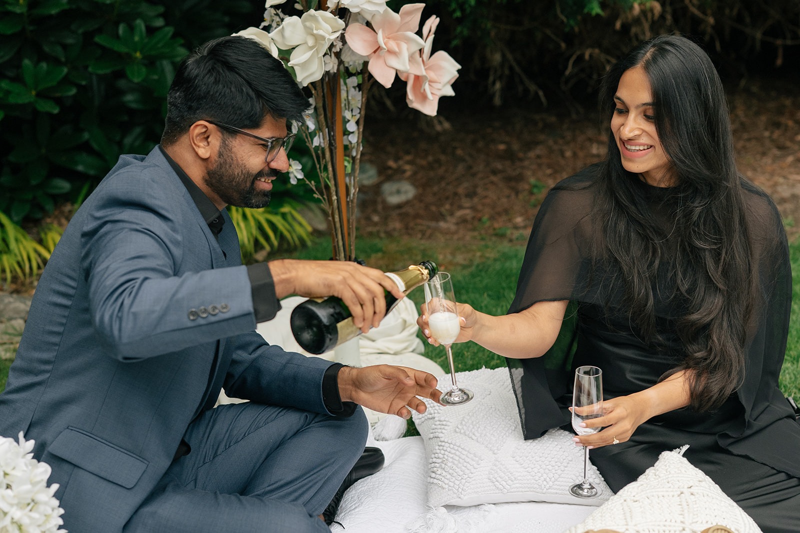 Piyush pours champagne into Priyanka's glass at their picnic celebration after his surprise proposal at Willows Lodge