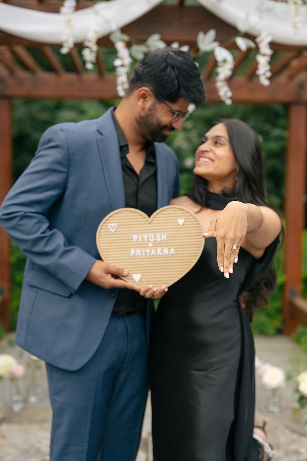 Priyanka shows off her engagement ring while holding a wooden "Piyush & Priyanka" heart sign after their Willows Lodge proposal
